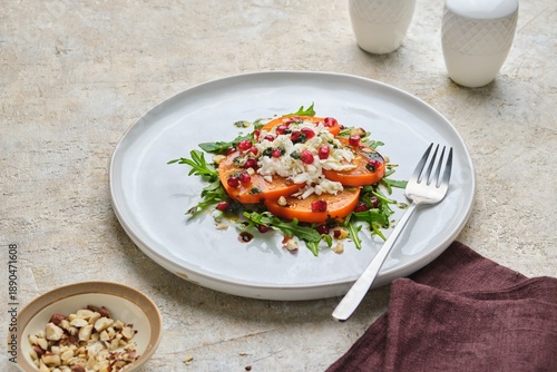 Persimmon salad with mozzarella and arugula on a gray ceramic plate against a light concrete background.