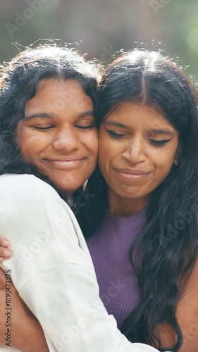 Affectionate close up portrait of two young Indian sisters embracing outdoors. Loving female siblings smiling and showing their strong bond