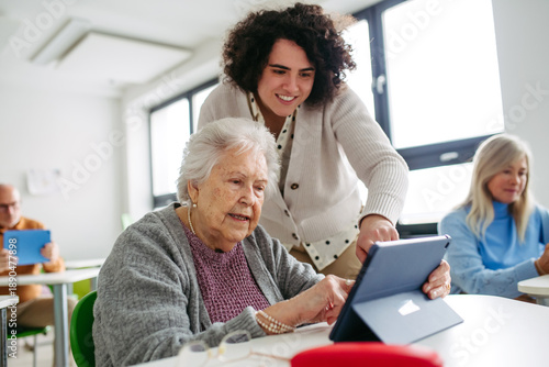 Bild auf Leinwand Elderly woman learning digital skills with tutor help.