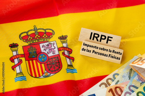 The word IRPF Impuesto sobre la Renta de las Personas Físicas (Spanish income tax) written on wooden blocks. The flag of Spain in the background. Financial business concept, Spanish language
