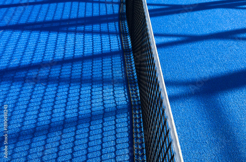 the blue synthetic grass surface of a paddle tennis court, near the net