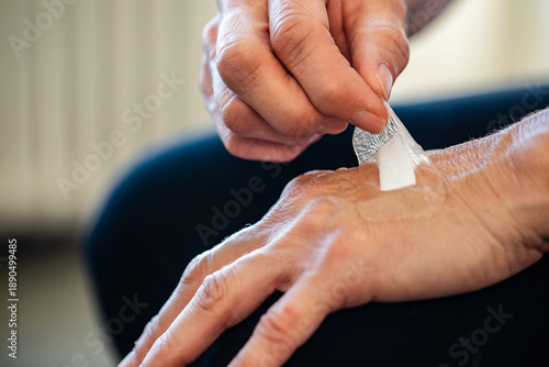 Bild auf Leinwand An elderly person removes a hydrocolloid bandage from their hand in a brightly l