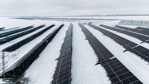 Aerial view of solar panels stretch across a snowy landscape, reflecting the muted sky, a stark contrast against the white fields, Sremska Mitrovica, Vojvodina, Serbia.