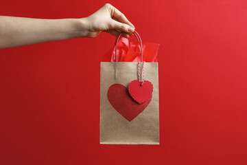 Woman holding gift bag with heart on red background, closeup. Valentine's Day