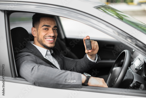 Принти на полотні Handsome young arabic businessman sitting inside auto and holding automatic key, renting nice car for business trip, side view, closeup, copy space