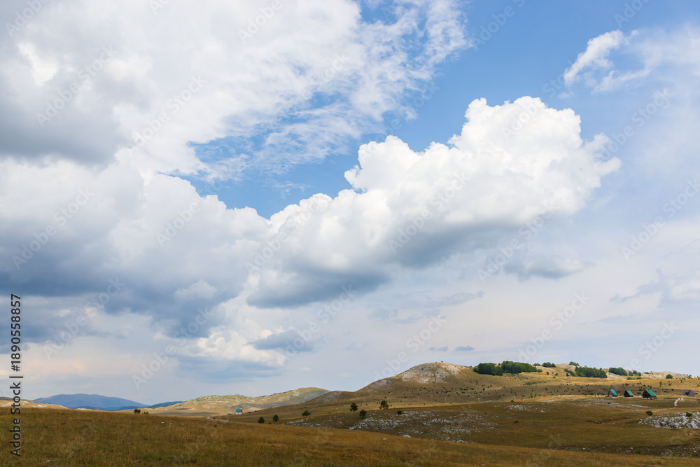 Obraz premium Dramatic clouds drift over rolling hills and a wide meadow