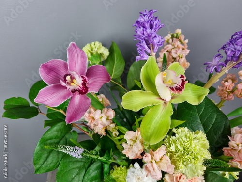 Photography Close-up of a vibrant floral arrangement featuring pink and green cymbidium orchids surrounded by soft pastel blossoms, purple hyacinths, and fresh green foliage