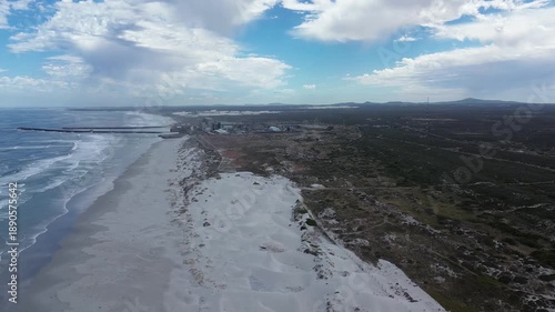 The camera moves sideways, right to left, over a pristine white beach and a nuclear power station on the coastline. 4K Aerial Video.
