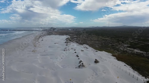 Camera rising up over a pristine white beach and a nuclear power station on the coastline. 4K Aerial Video.