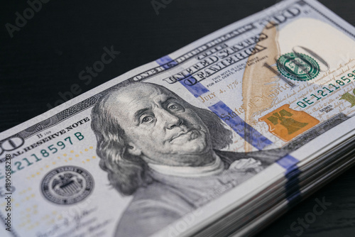 Photos US dollar banknotes stacked on a dark surface, featuring detailed imagery of Ben