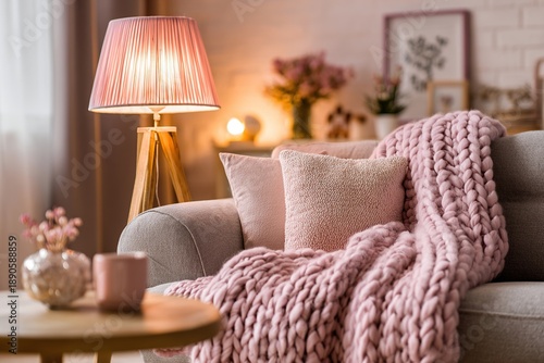 A cozy living room scene illuminated by a warm lamp, featuring a comfortable gray sofa, a knitted throw, and decorative pillows, creating a relaxing and inviting atmosphere.