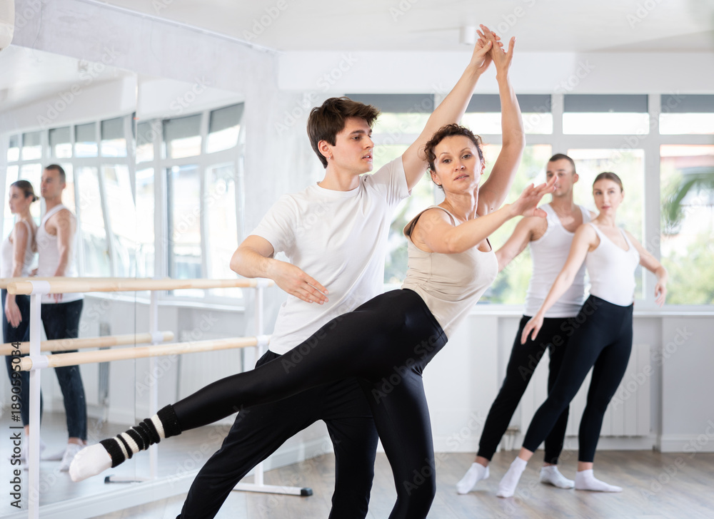 Fototapeta premium Young guy and adult woman perform paired ballet dance in studio