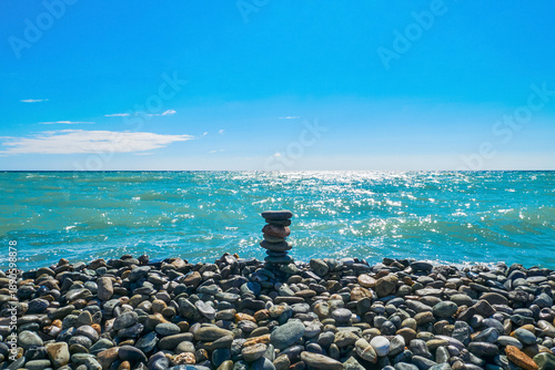 A pyramid of stones on a pebbly sea beach, against the background of the blue sea. Beach holidays at the resort. The concept of harmony, unity with nature, meditation.