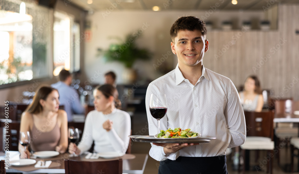 © JackF - Young male waiter posing with tray of salad and wine in restaurant