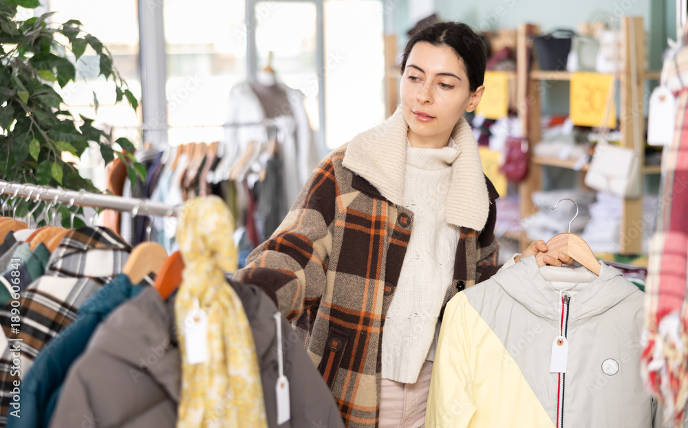 Obraz premium Girl chooses coat or jacket for the winter period in a fashionable clothing store