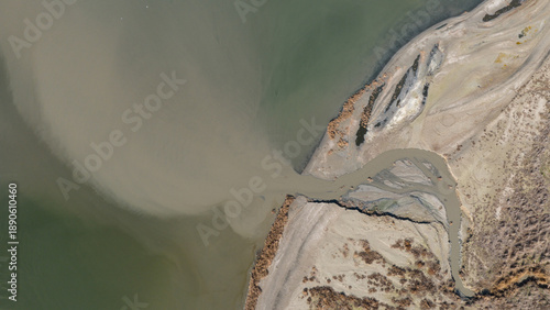 Картината върху платно Drone view of a small river delta carrying sediment and industrial waste into a larger body of water, showing water pollution
