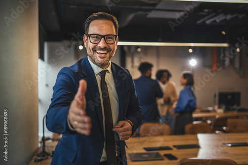 Tablou pe pânză Smiling businessman offering hand for handshake in modern office
