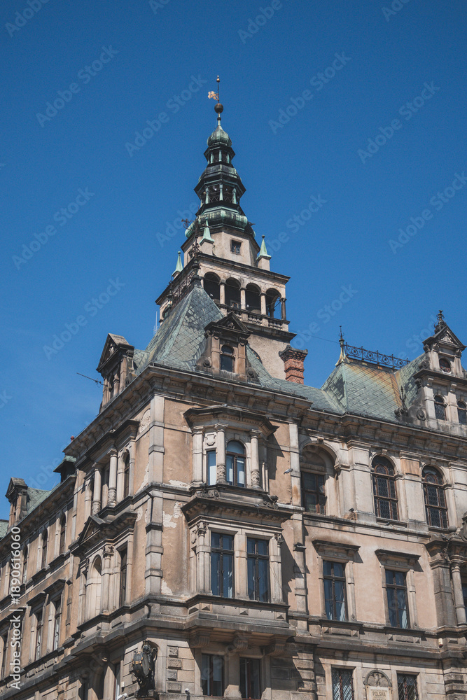 Fototapeta premium Low angle architectural detail of an ornate Neo-Renaissance corner building in the historic center of Kłodzko. The facade features intricate sculptures, decorative reliefs, and a prominent balcony typ
