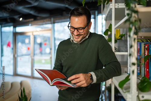 Cuadro en lienzo Smiling man reading book in modern office library