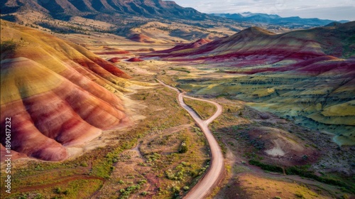 Colorful hills showcase shades of red yellow and brown in eastern Oregon. A winding road meanders through this unique geological marvel surrounded by mountains.