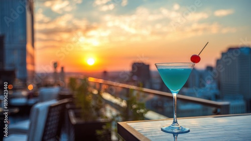 A refreshing cocktail sits on a table overlooking a stunning sunset. The vibrant colors of the drink and the golden sky create a serene atmosphere in the city.