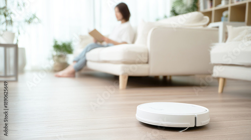 ロボット掃除機が稼働するリビングのソファで読書をしてくつろぐ女性

