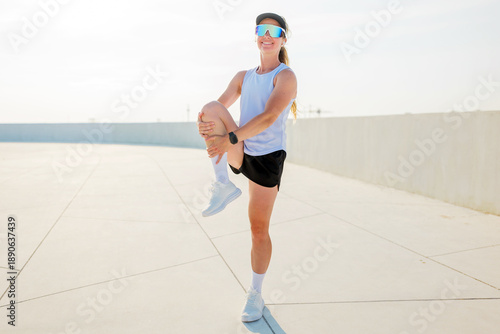 Принти на полотні Woman stretches her leg while practicing fitness in a bright outdoor setting dur