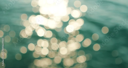 Soft golden bokeh circles dance on deep blue water surface in bright sun