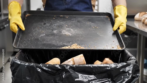 Discarding stale bread and baked goods into a black trash bag in a professional kitchen setting, Wasteful disposal of unsold bakery items