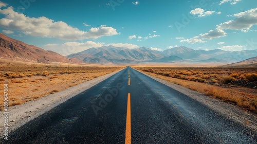 Open Road to Adventure: An endless stretch of asphalt guides the viewer's eye towards the majestic mountains under a boundless, clear, bright blue sky. It is the beckoning call for adventure.
