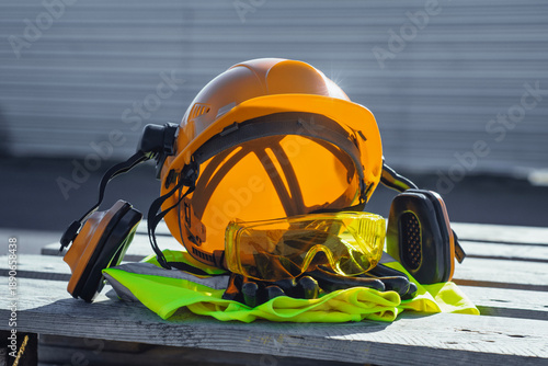 Cuadro en lienzo Orange hard hat with ear muffs for hearing protection with yellow safety goggles, work gloves and a rolled-up neon green high-visibility vest with reflective stripes