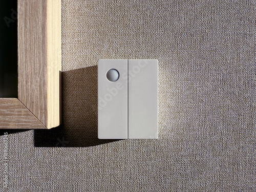 A white rectangular wall mounted occupancy sensor with a circular passive infrared lens sits on a tan textured wallpaper surface
