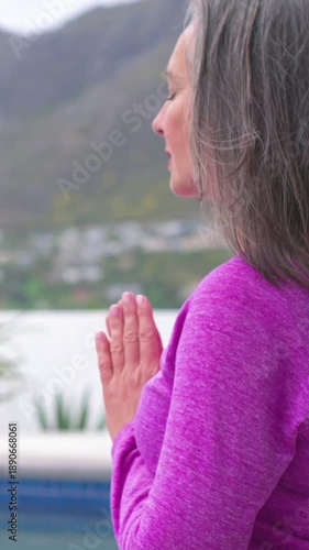 Vertical video: Praying woman raising chin breathing lowering hands meditating poolside, copy space