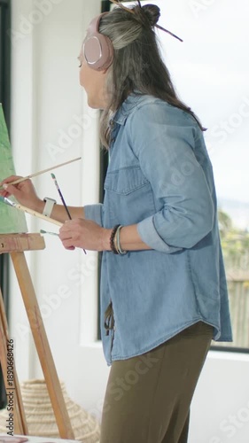 Vertical video: Painting artist in denim at home easel with palette, sunlight drawing brush strokes