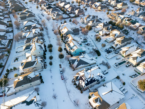 Photos Drone aerial view of residential suburb with single-family homes covered in fresh snow on roofs, yards and streets under clear winter sky