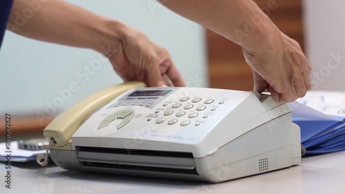 A man hands using a fax machine, placing paper into the tray and sending a fax in an office