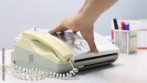 A man hands using a fax machine, placing paper into the tray and sending a fax in an office