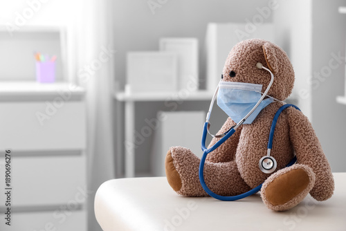 Toy bear with medical mask and stethoscope on couch in pediatrician's office