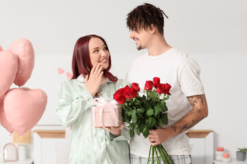 Young lovely couple greeting each other with gift and bouquet of roses at home. Valentine's Day celebration