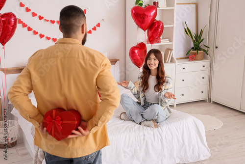 Quadro em tela Young man hiding heart-shaped gift for his girlfriend behind back in bedroom