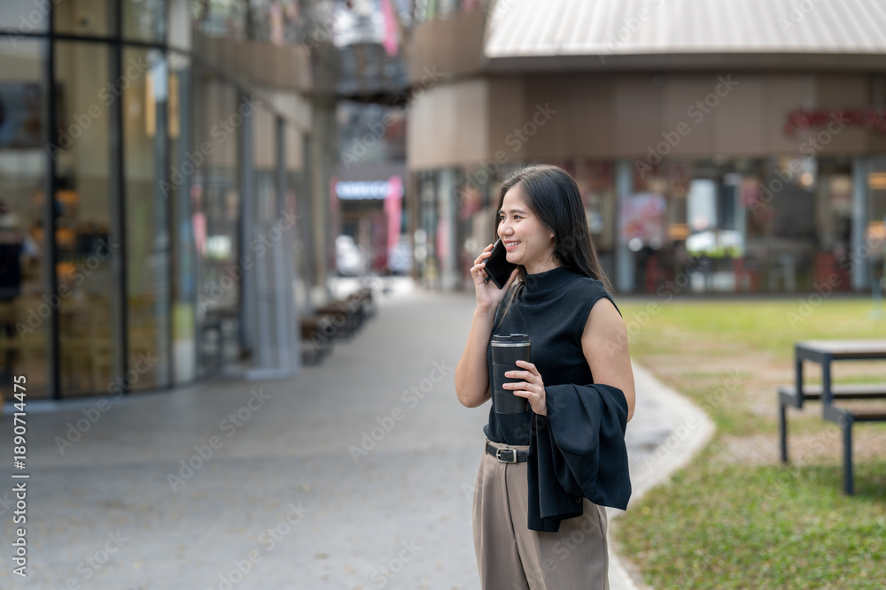 Fototapeta premium Asian woman smiling talking on phone holding coffee