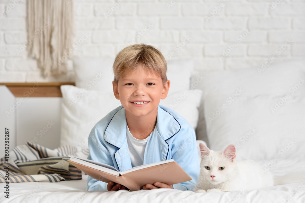 Obraz premium Cute little boy with cat reading book in bedroom