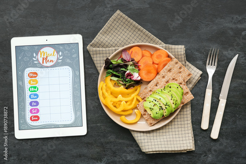 Tablet with meal plan and fresh vegetables on grunge black background