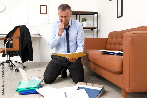 Worried mature businessman reading documents while biting nails in office