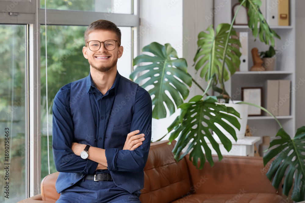 Fototapeta premium Handsome young happy businessman in eyeglasses sitting on sofa at office
