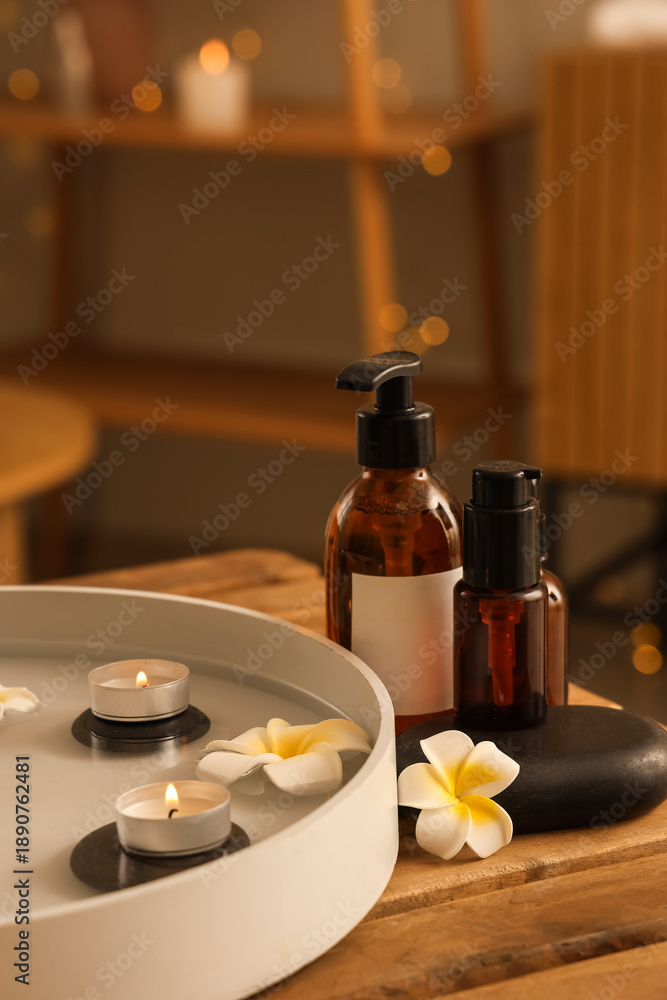 Obraz premium Plate with candles, spa stones, plumeria flowers and cosmetic products on table in salon
