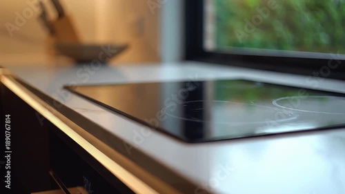 Smooth camera pan across a modern kitchen countertop featuring an induction cooktop and ambient lighting, showcasing contemporary interior design and lifestyle.