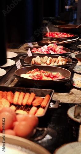 Assorted breakfast dishes in cast iron pans at hotel buffet. Sausages, bacon, eggs, hash browns. Person serving food. Warm lighting, professional catering setting Vertical.
