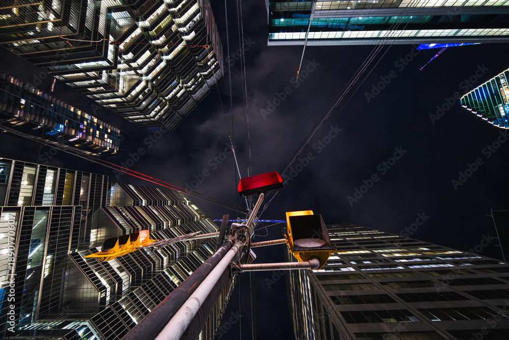 Naklejka premium A red traffic signal hangs like a suspended ember between towering glass facades, while cables radiate from the pole like the strings of a giant urban instrument.