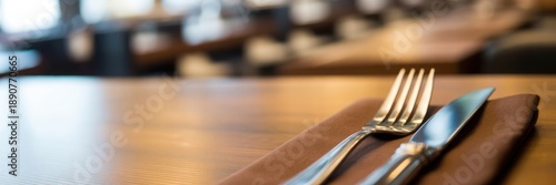 Table setting with a fork and knife on a brown napkin on a wooden table, suitable for restaurant, dining, and culinary themes.